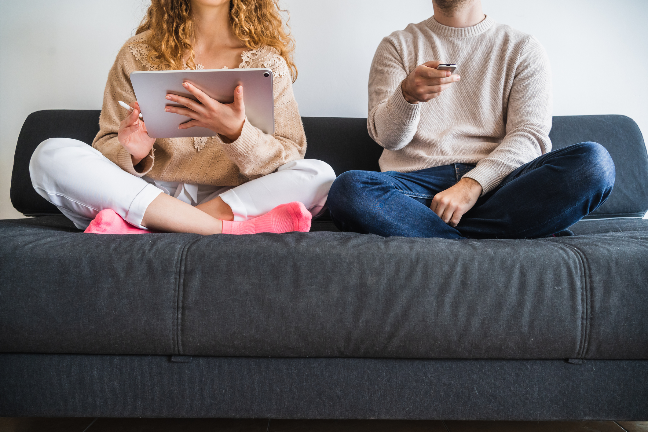 Crop couple resting on sofa using tablet and tv remote