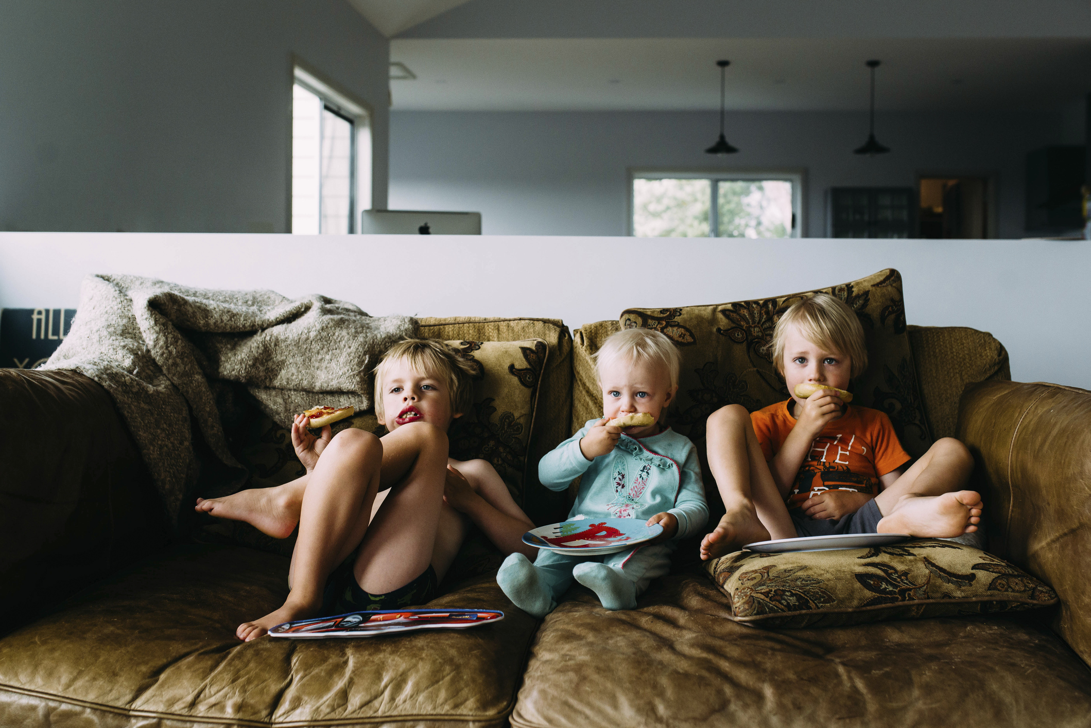 Siblings eating snacks watching TV while relaxing on sofa at home