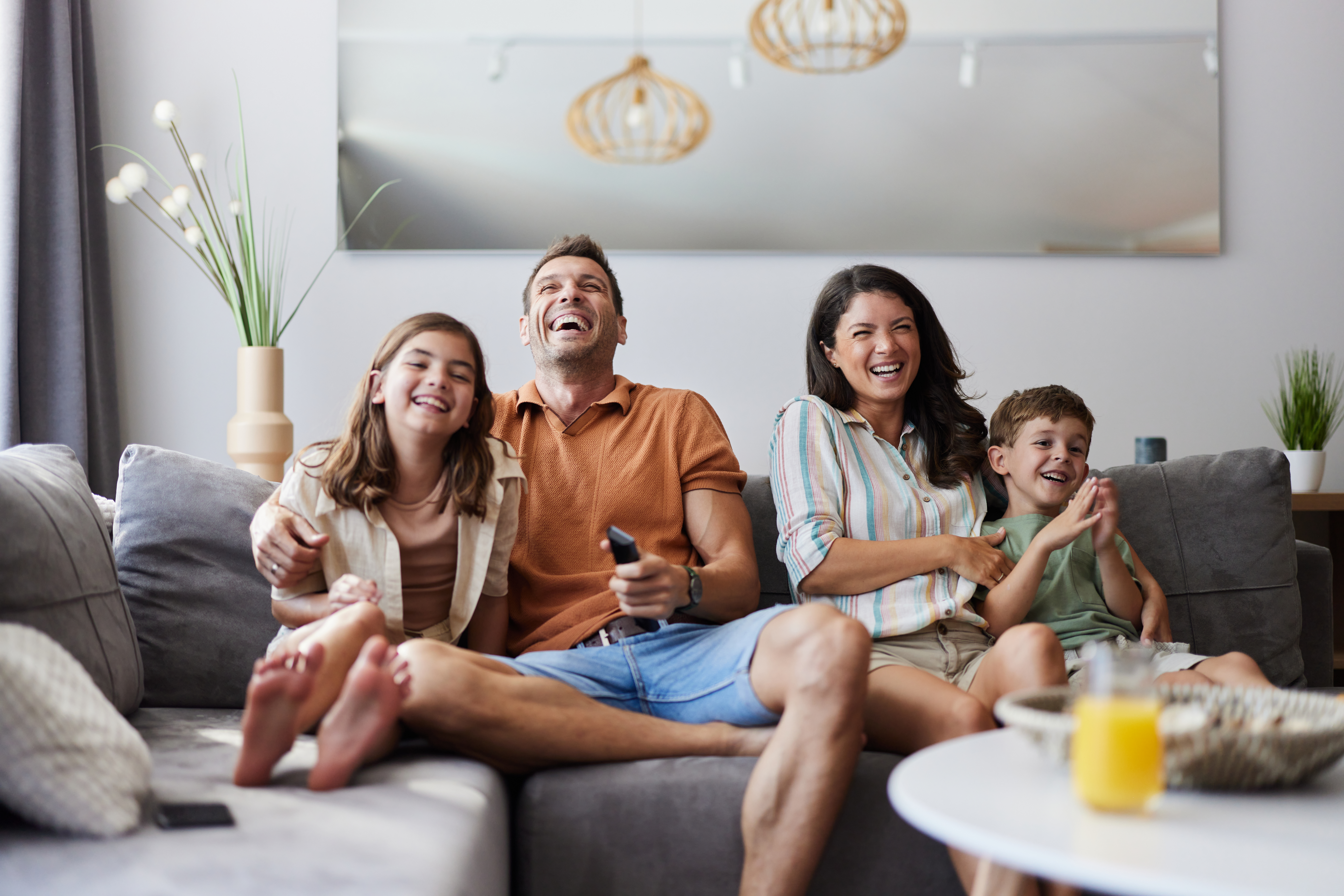 Cheerful parents and their kids having fun while watching a movie on sofa in the living room.