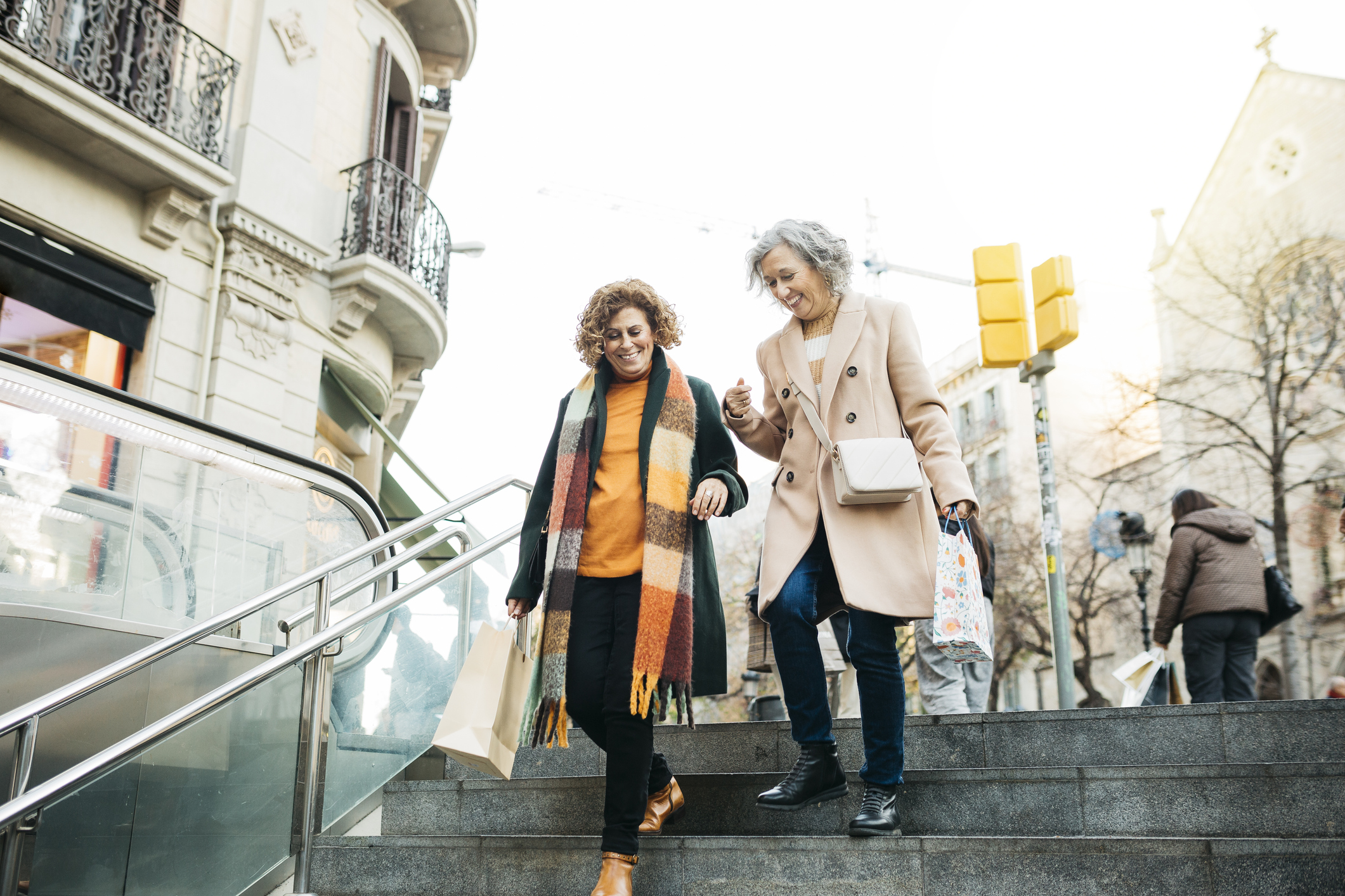 Female senior smiling couple walking down the stairs of the metro carrying shopping bags