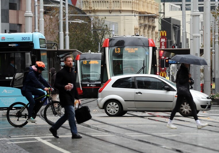 Pedestrians and a cyclist cross road as vehicles pass trams sitting at a junction in the central business district of Sydney, Australia, on Monday, May 25, 2020. Australia has a three-stage plan to reopen the economy by the end of July, after lockdown restrictions smashed businesses, particularly in the hospitality and services industry. The nations eight state and territory governments are moving at their own pace, depending on the number of Covid-19 infections in their jurisdictions. Photographer: Brendon Thorne/Bloomberg