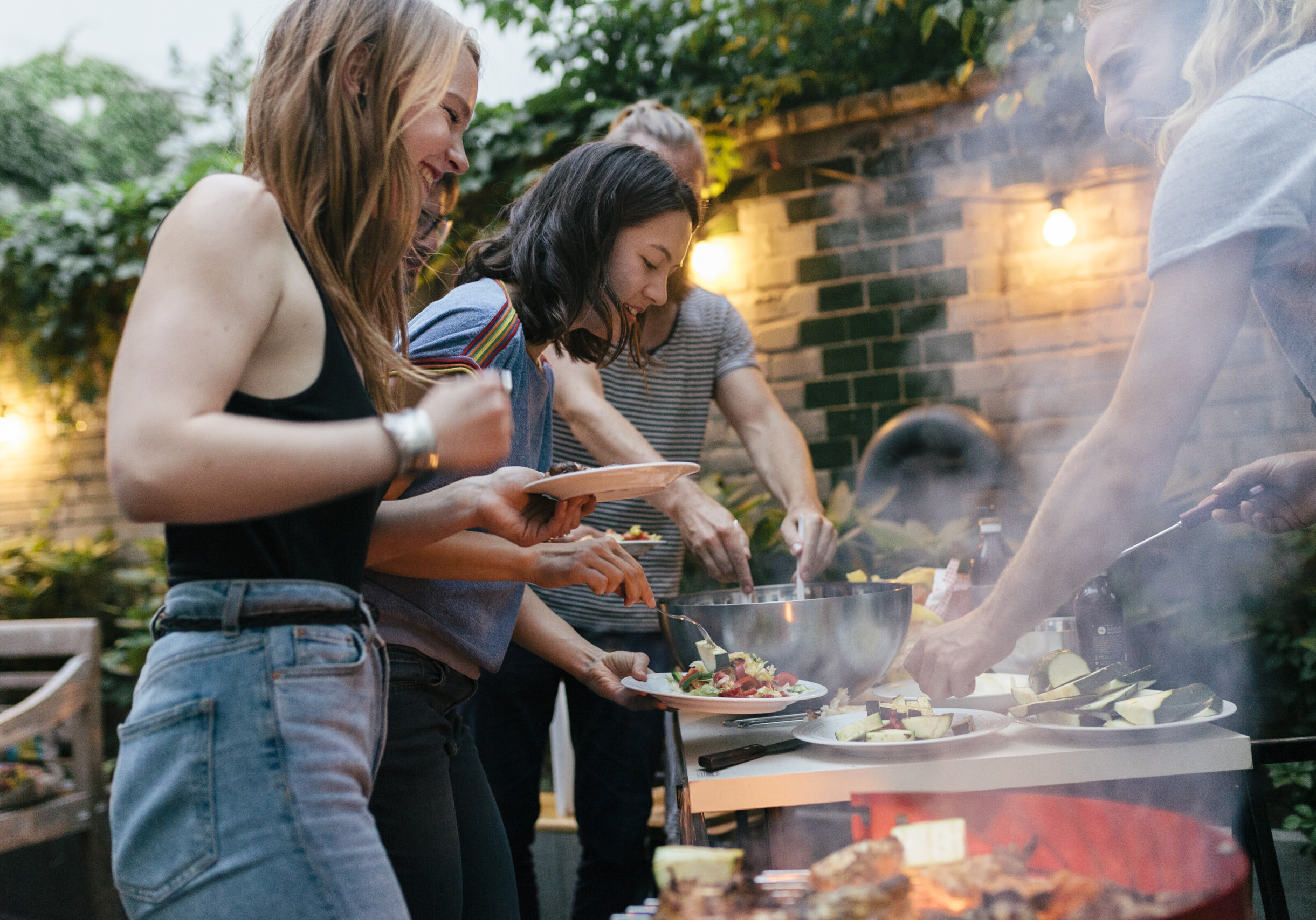 A young group of friends are helping themselves to freshly prepared food at a summer evening Barbecue.