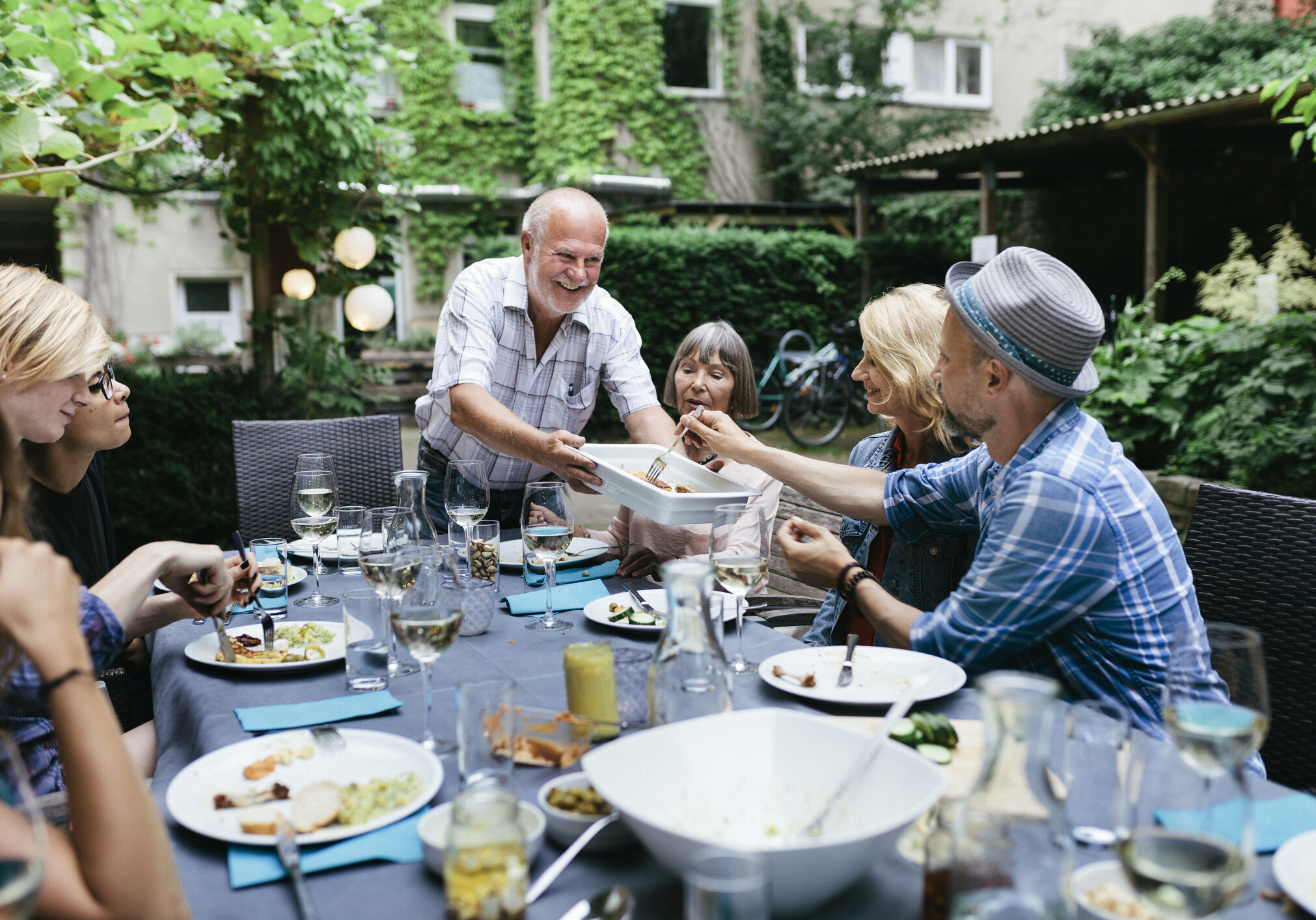 A family sharing food at a large table during a barbecue in a courtyard together.