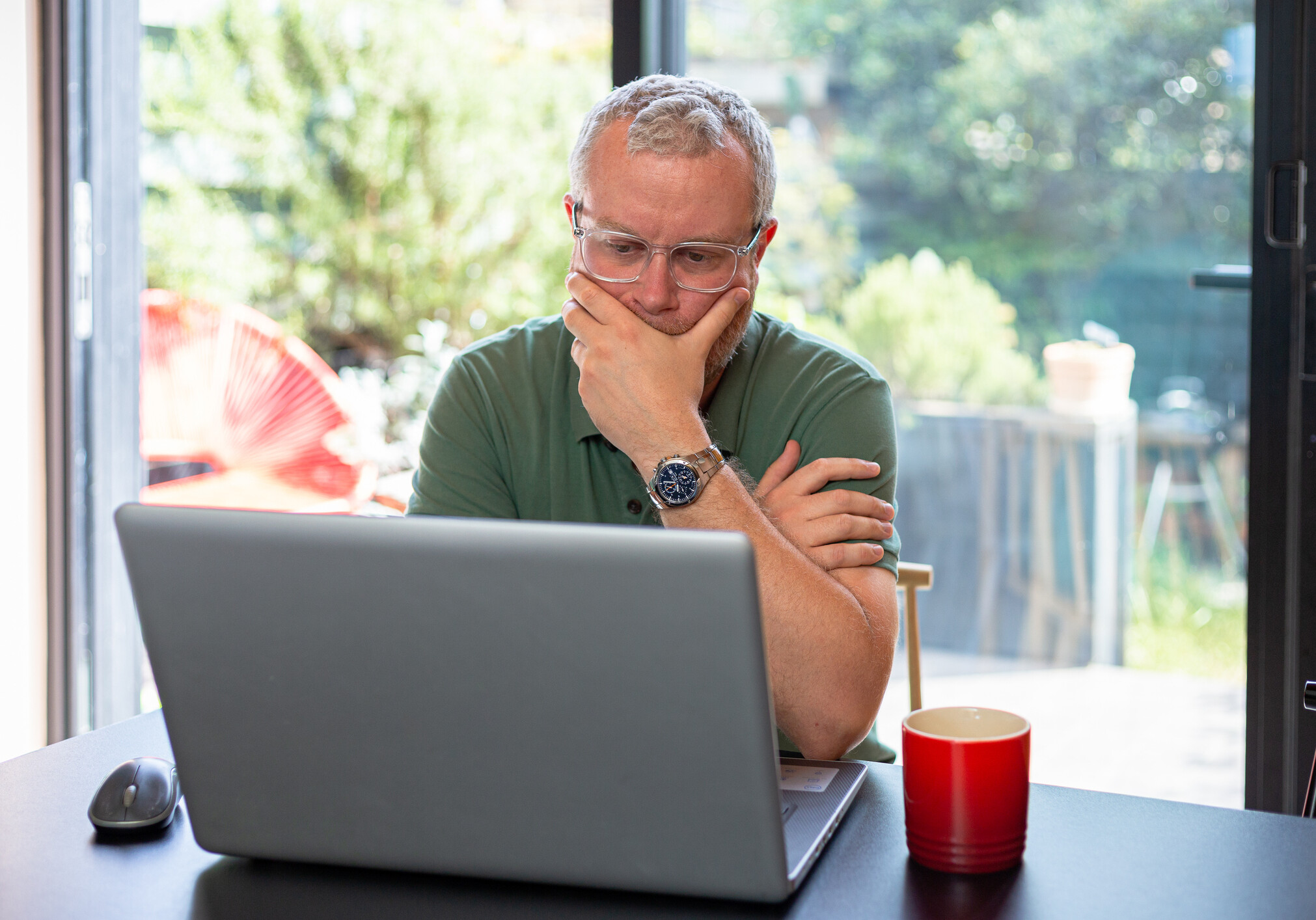 A worried man touches his face in an anxious way after looking at bad news on his laptop.