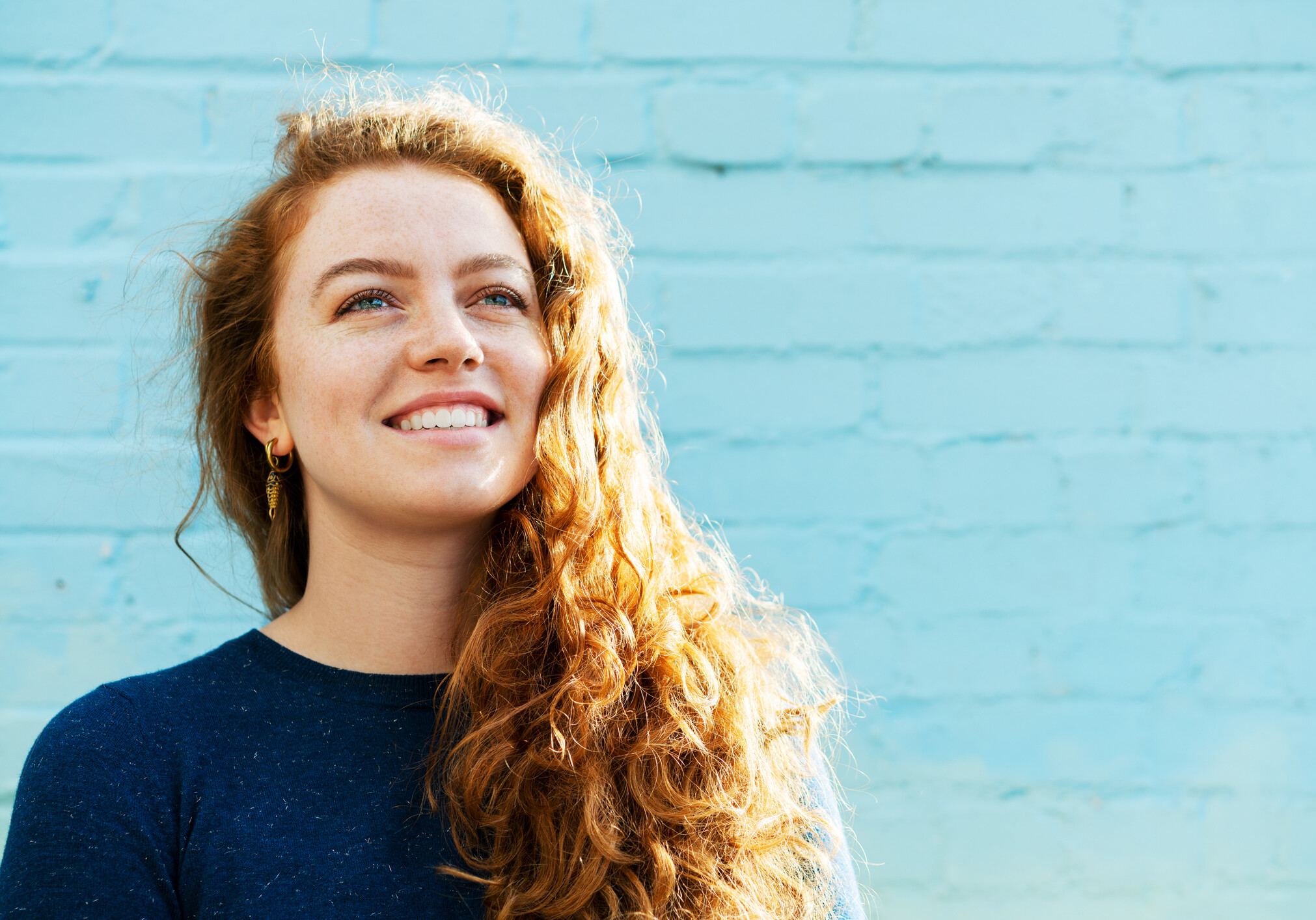 Woman looking up, smiling next to blue back wall