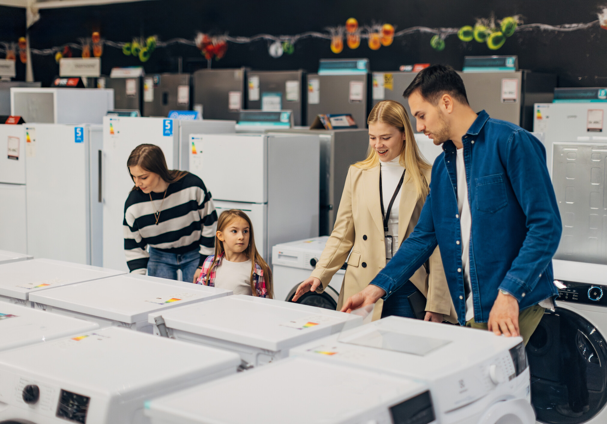 The smiling saleswoman shows home appliances to a young couple who came to furnish their new apartment