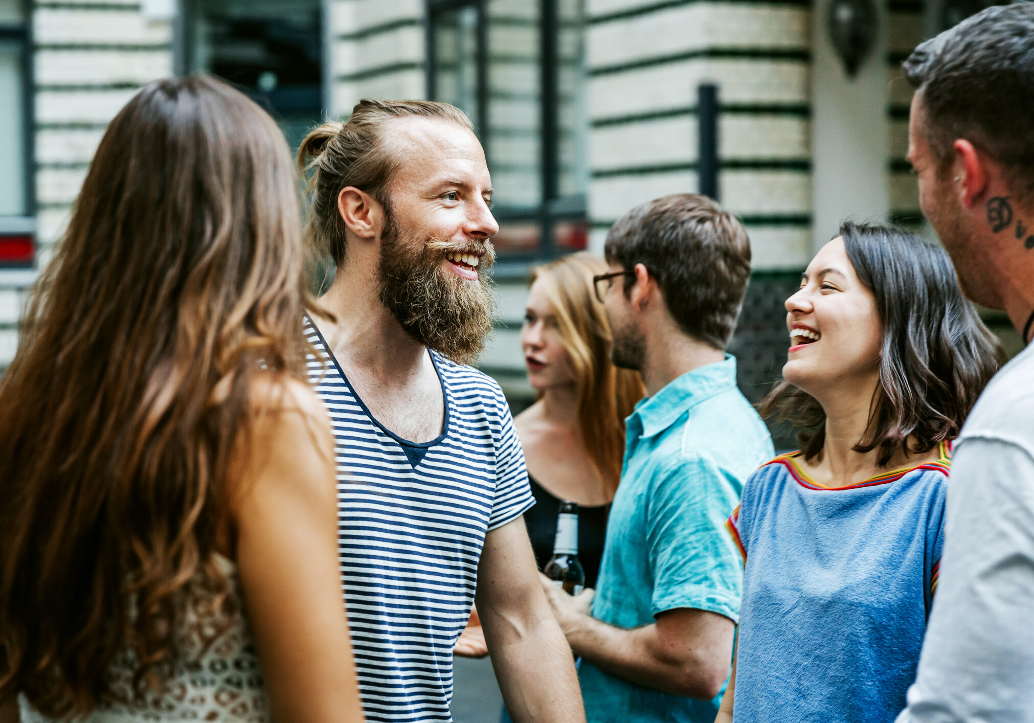A young group of friends meeting together at a barbecue are chatting and smiling as they greet each other.