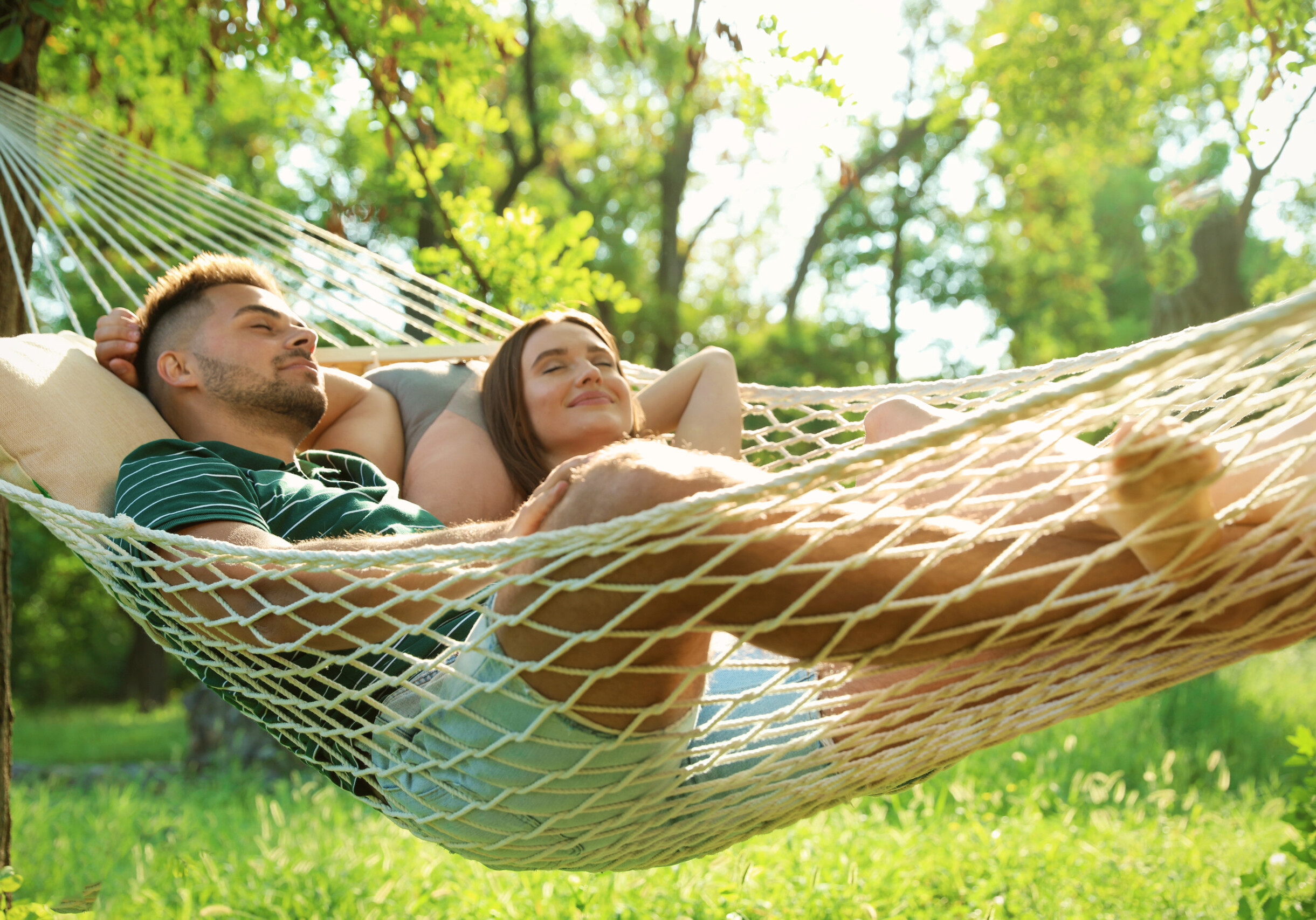 Young couple resting in comfortable hammock at green garden